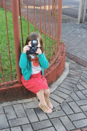 a little girl takes a picture while sitting on the side walk