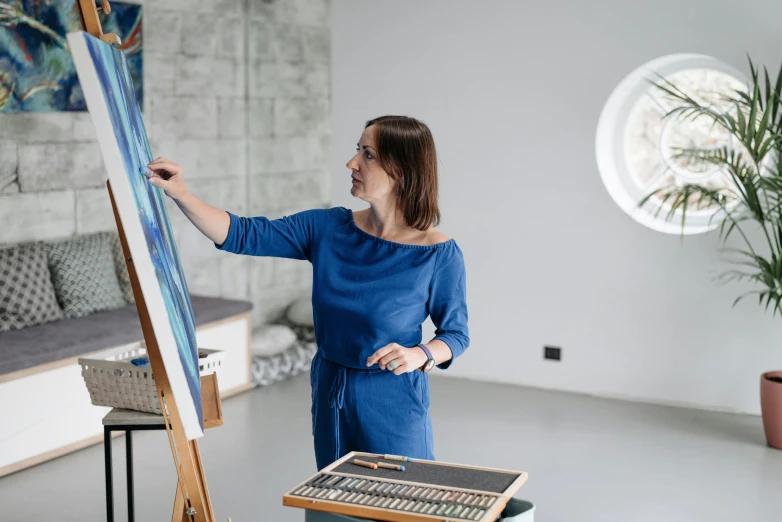 the woman is standing in front of the easel looking at the paintings