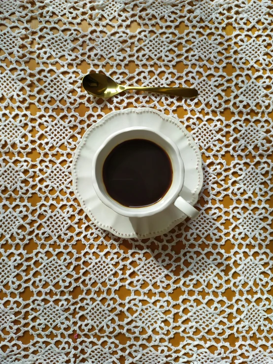 a cup of coffee on a doily cloth with spoons