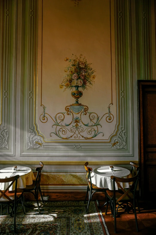 a white wall with a painting behind two chairs