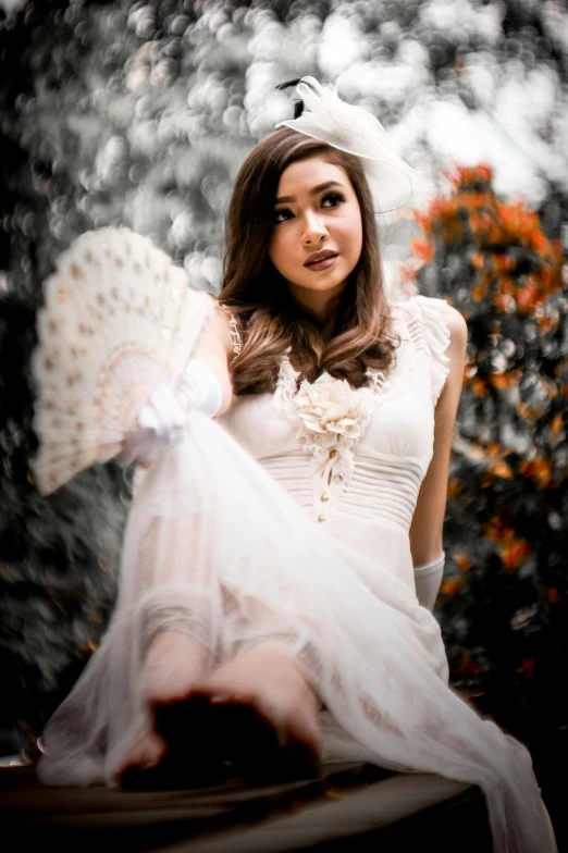 a woman in white holds a fan while posing