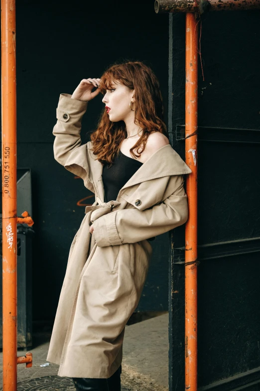 the woman wearing a coat and boots poses in an orange frame