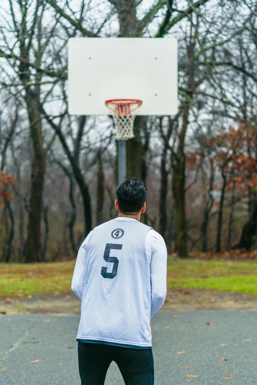 a man standing by a basketball hoop with trees in the background