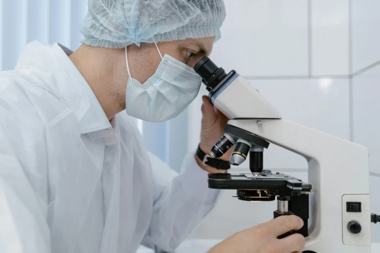 a man wearing white holding a microscope while staring into it