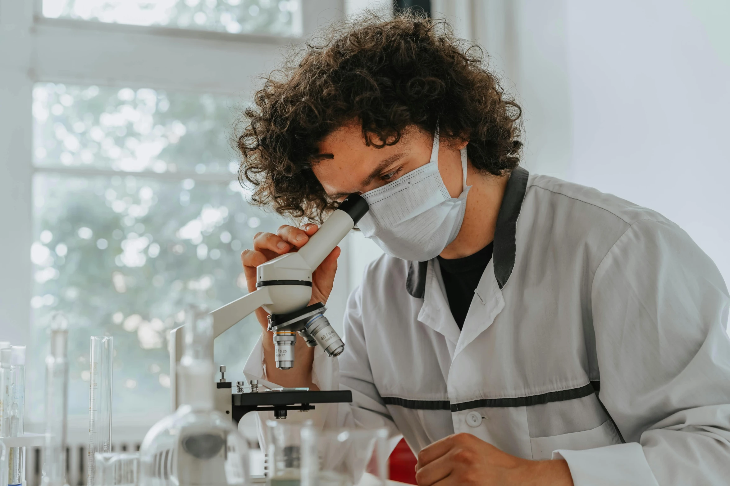 a young man wearing a surgical mask looking at a microscope