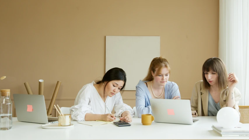 three girls look at laptops sitting on a table