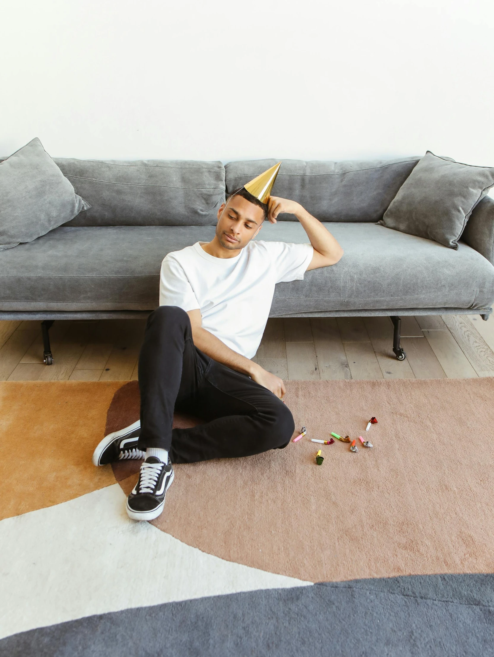 a young man sitting on the floor and holding his head with a yellow party hat