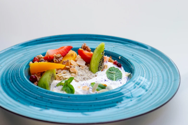 a plate has a colorful salad with strawberries, kiwi, bananas and yogurt