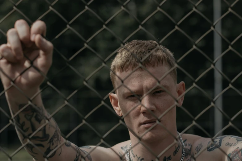a man holding onto his wrist while behind the chain link fence