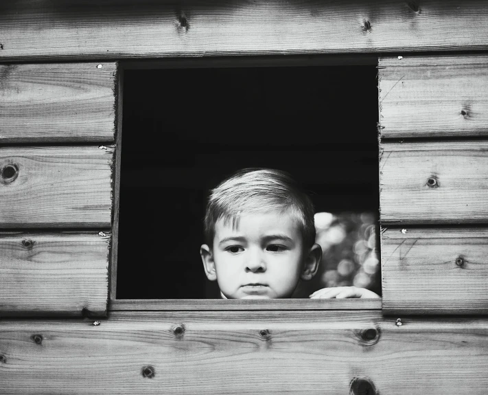 a small boy looking out the window of a wooden structure