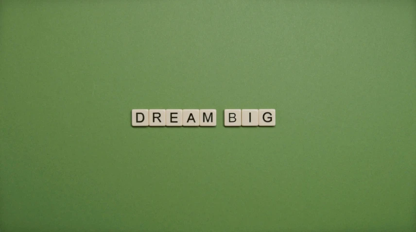 scrabble letters spelling out the word dream big, on a green background