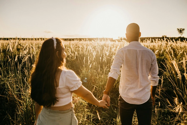 a man and woman walking in tall grass holding hands