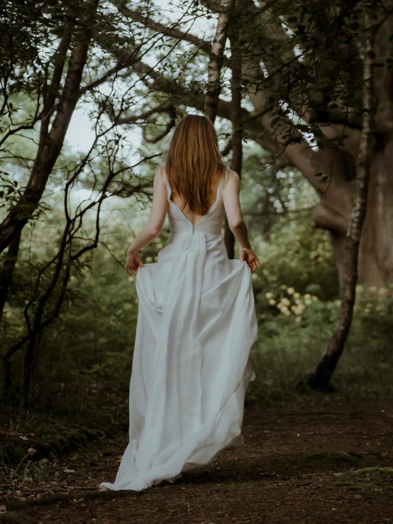 a woman in a long dress walking through a forest