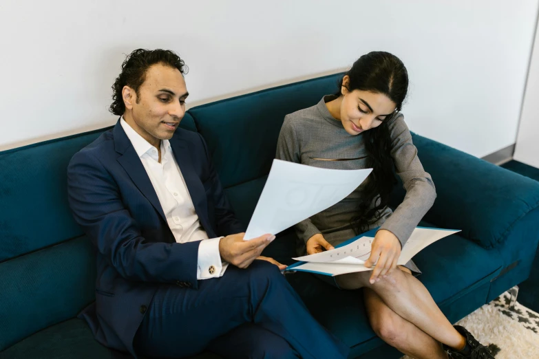 a man and woman sitting on a couch looking at papers