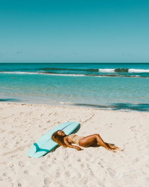 a female laying on a beach with a surfboard in the sand