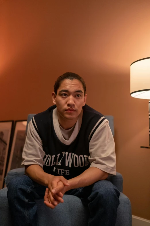 a young man in a white shirt is sitting on a chair