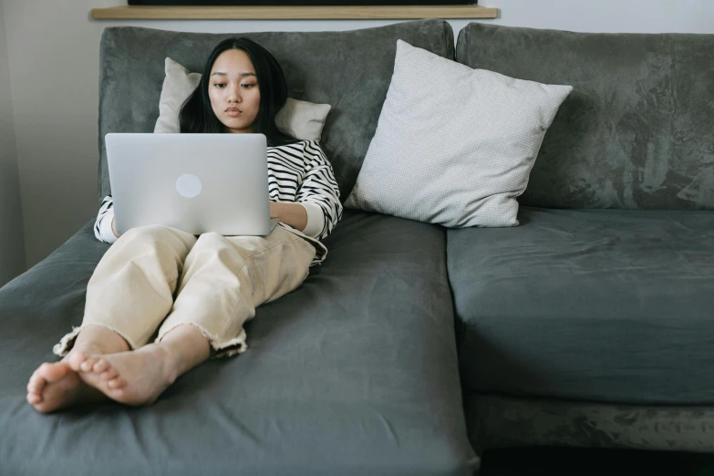 a young woman laying on the couch using a laptop