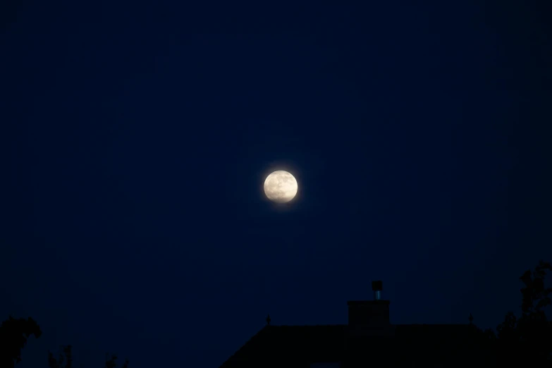 full moon setting over a large residential house roof