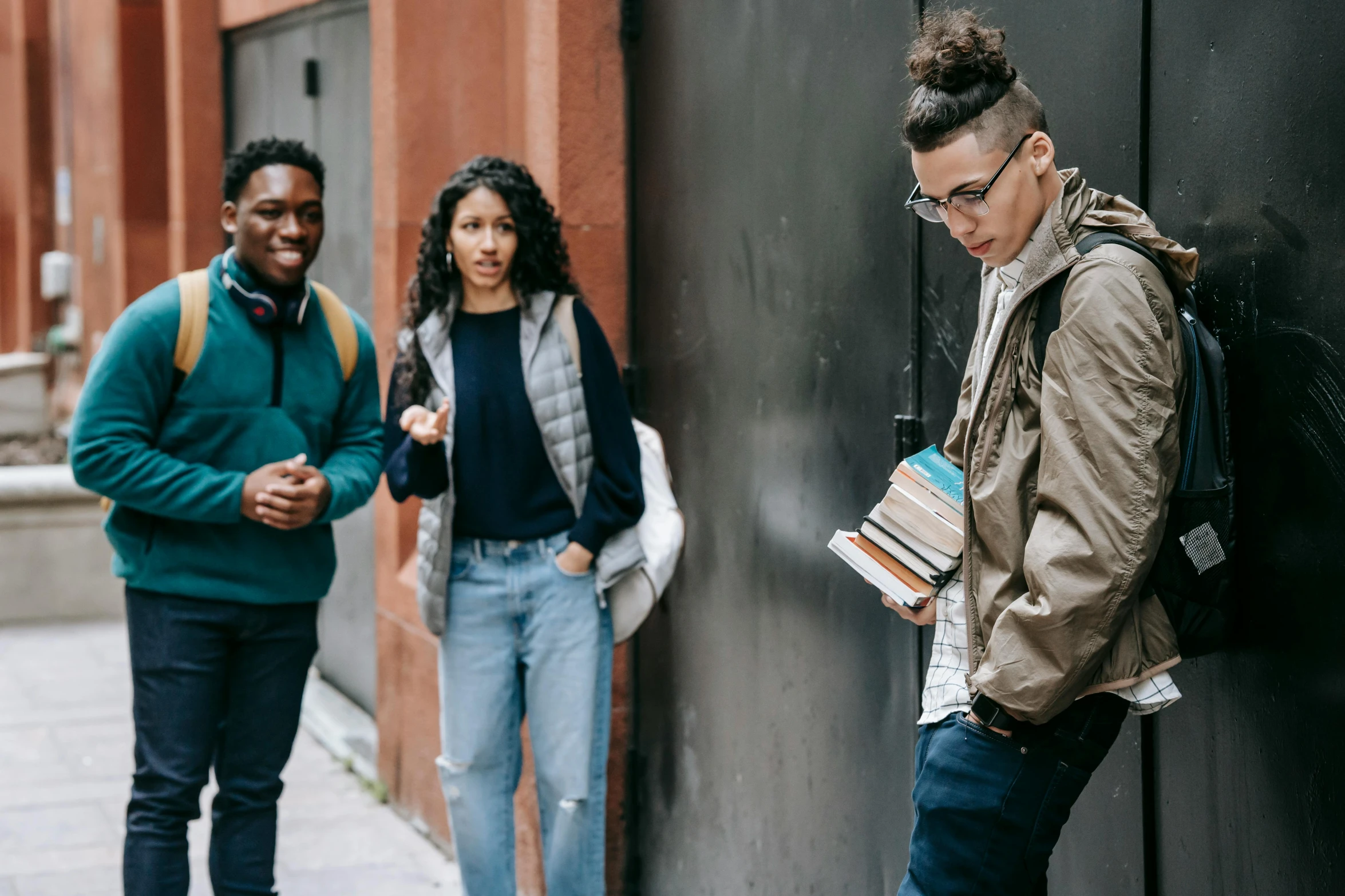 three young people looking at books near a wall