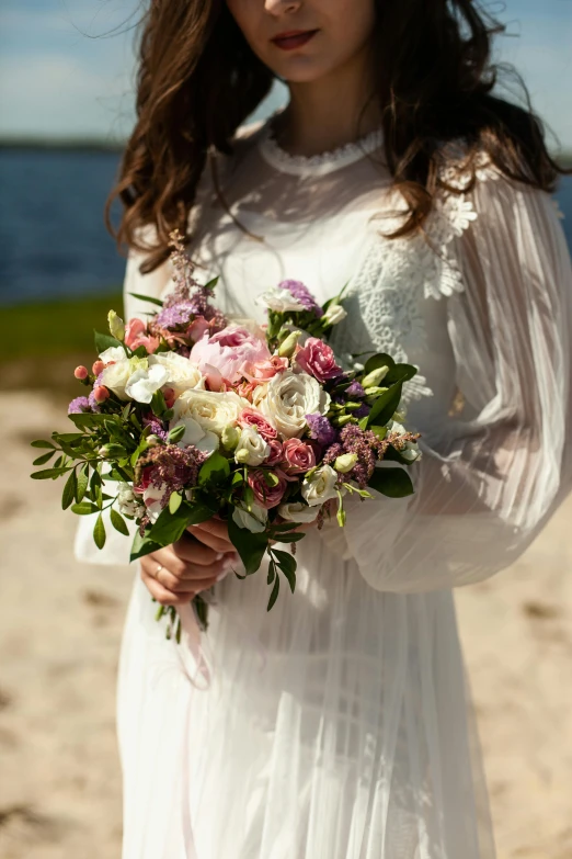 a young woman standing on the beach holding a bouquet of flowers