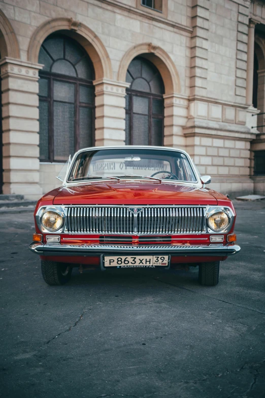 a red car sits parked in a lot near an old building