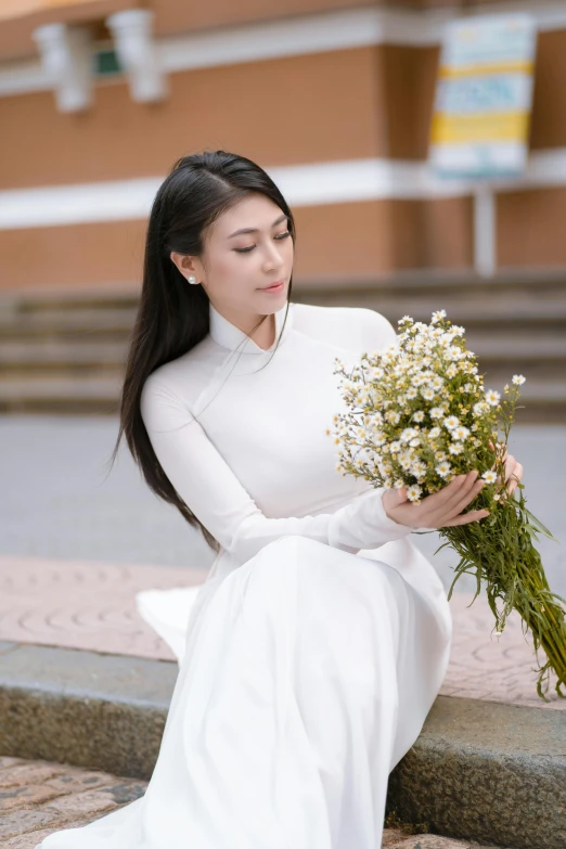 the woman wearing a white dress is holding flowers