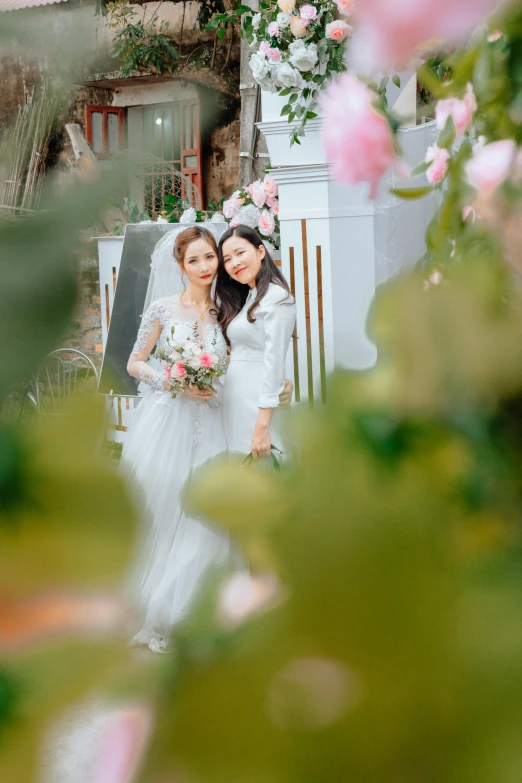 two brides pose in the background of greenery