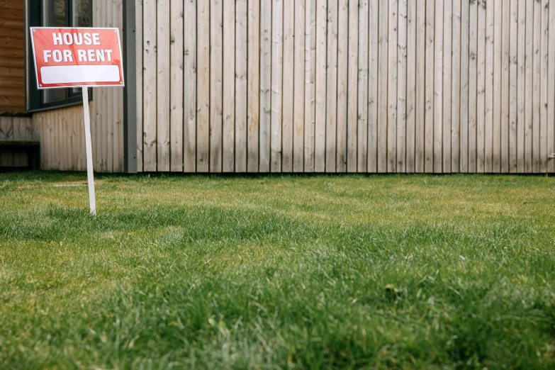 a red house for rent sign standing in the grass