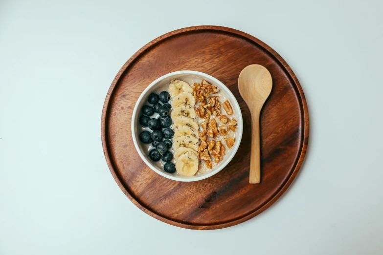 the bowl has bananas, blueberries, nuts and a spoon