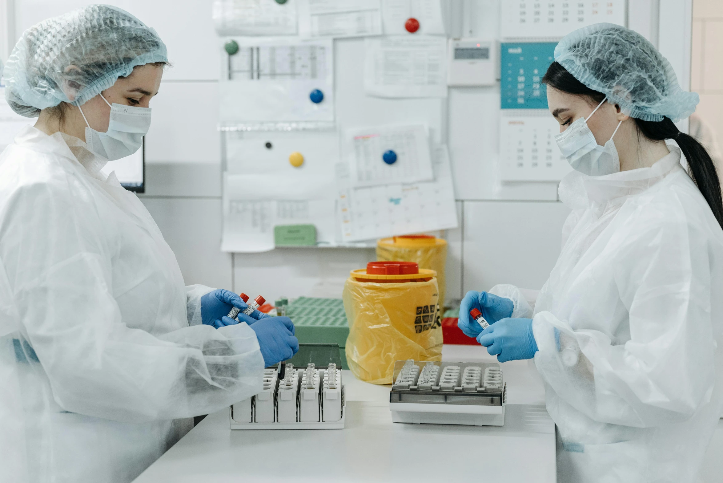 two people in white lab coats and masks one of them holding a yellow jar while the other hand is pointing to a computer