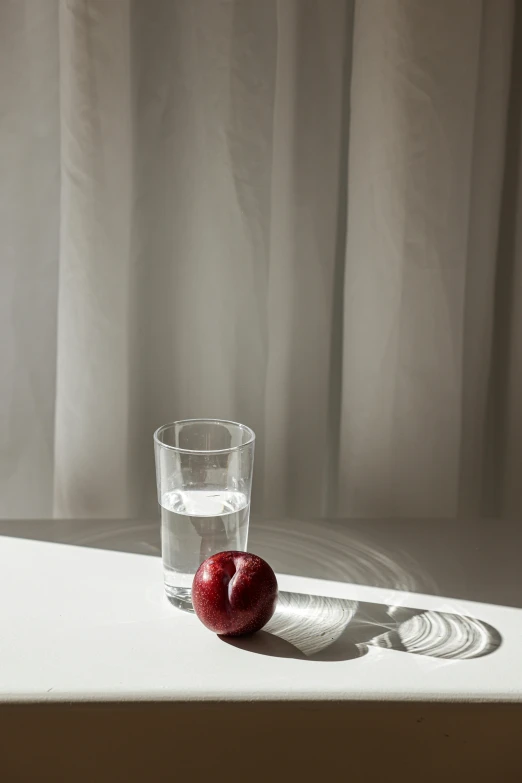 a glass and an apple on a table in the sunlight