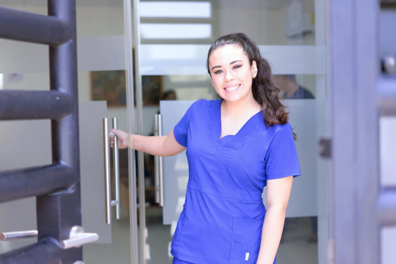 the smiling nurse poses with her hand out and opens the door