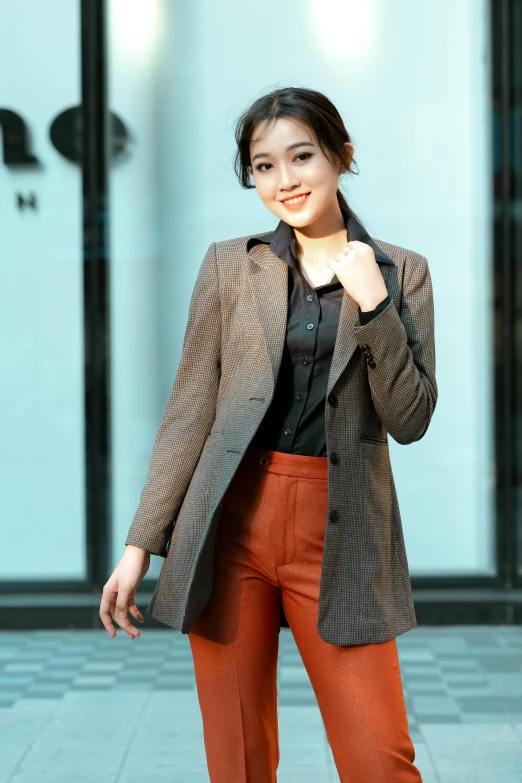 a woman posing on a city street while wearing a jacket and orange pants