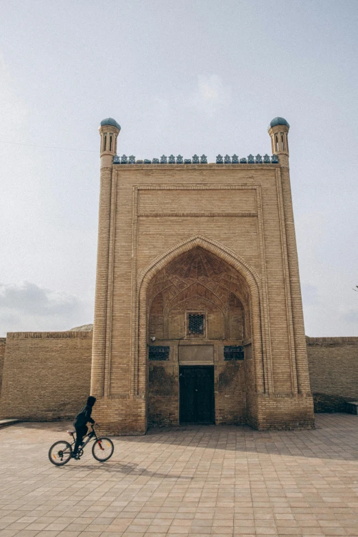 man rides bicycle in front of a tall stone structure