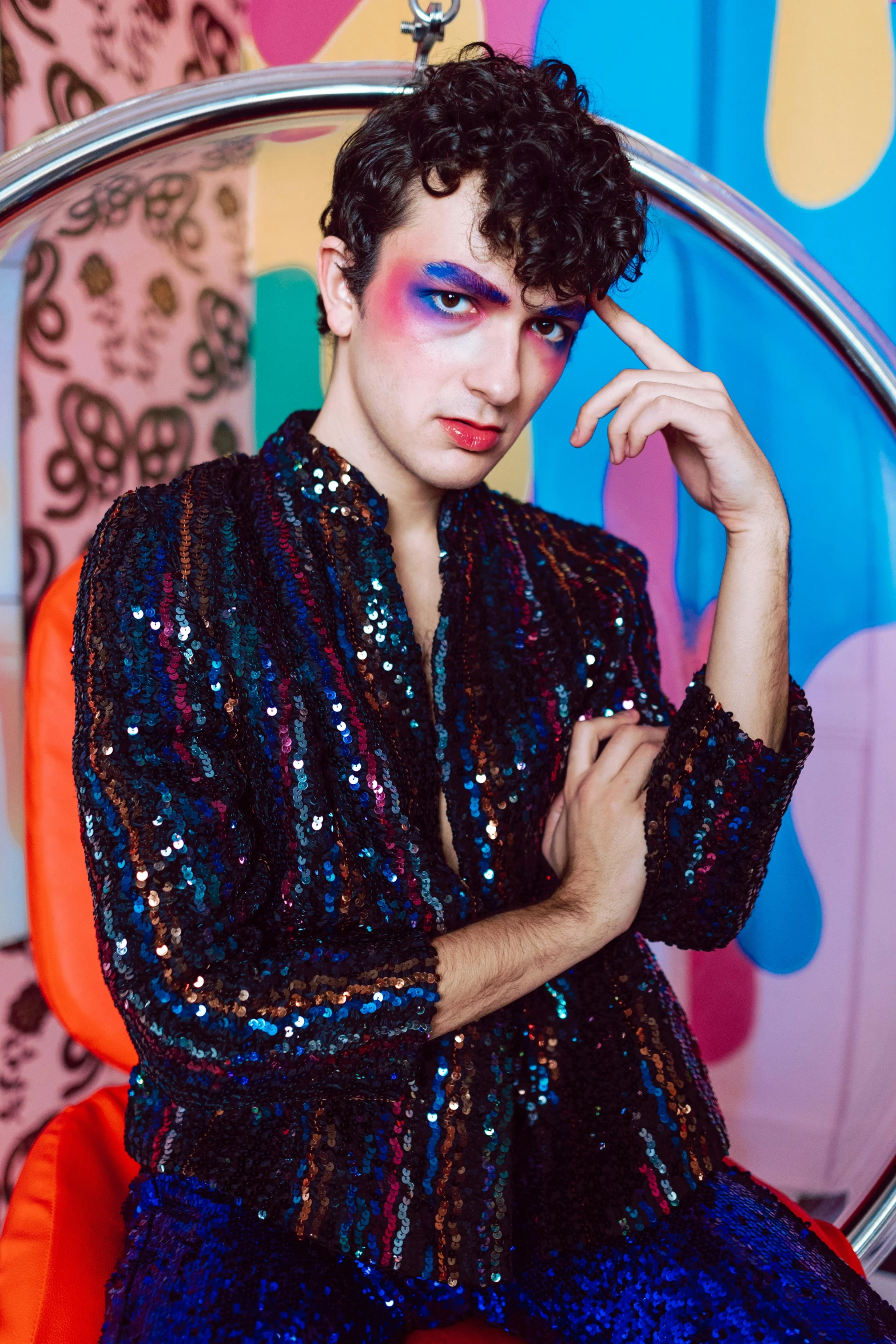 a young man sitting in a chair wearing a rainbow makeup
