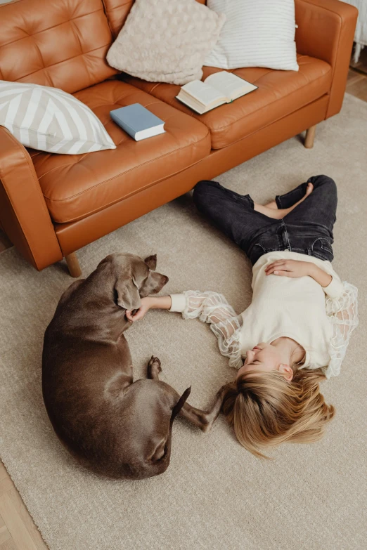 a girl laying down with two dogs by a couch