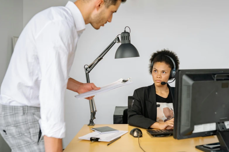 the woman is sitting in front of her desk as a man stands behind her and looks up