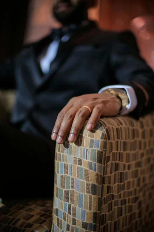 a close up of a man in a tuxedo with his hands on the arm of a chair