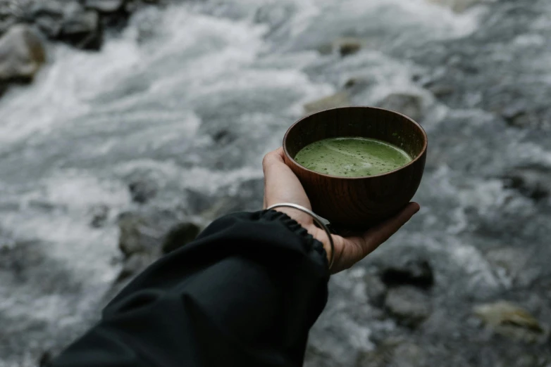 a hand holding a small wooden bowl filled with liquid