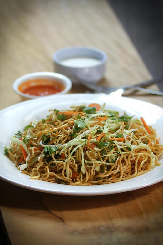 a plate of noodles, carrots and broccoli with sauce on the side