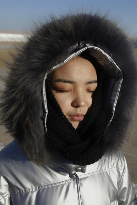 a woman wearing a silver jacket with an ear flap in a field