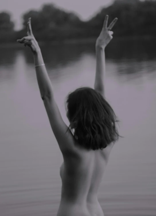 the woman has her arms up in the air while standing next to a body of water