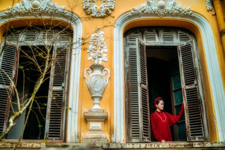 woman in red standing at window sill with vase in front of her