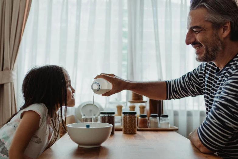 a man pouring water onto a cup with a little girl