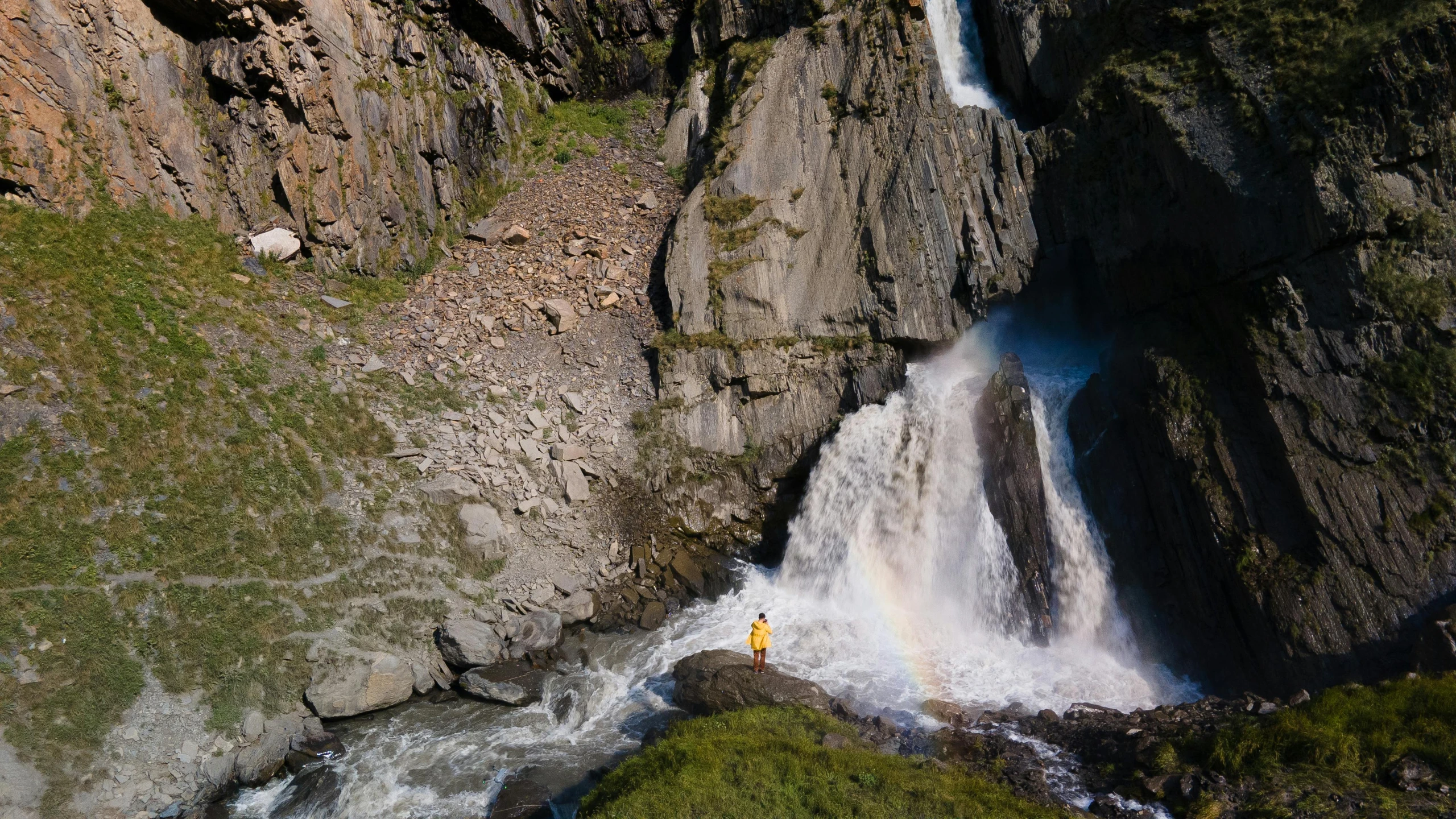 a man standing next to a waterfall and a rainbow