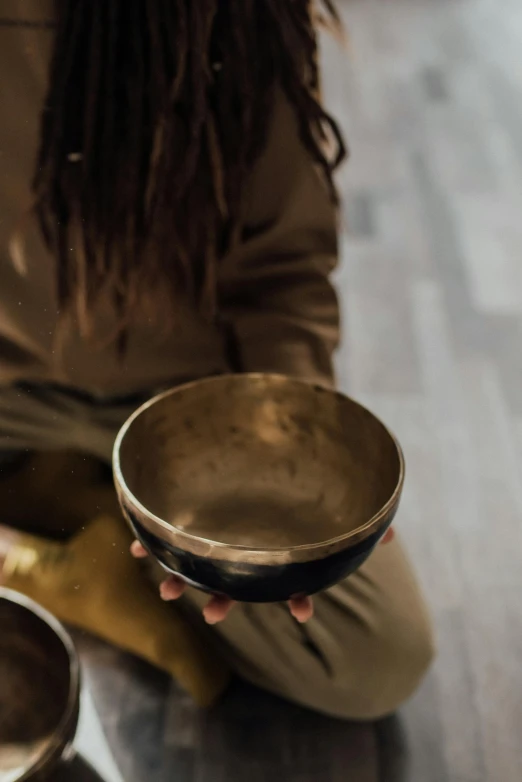 a woman sits on the floor while holding a metal bowl