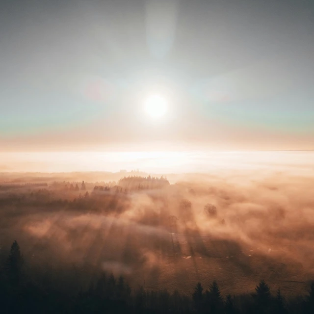 the sun shining over a foggy landscape