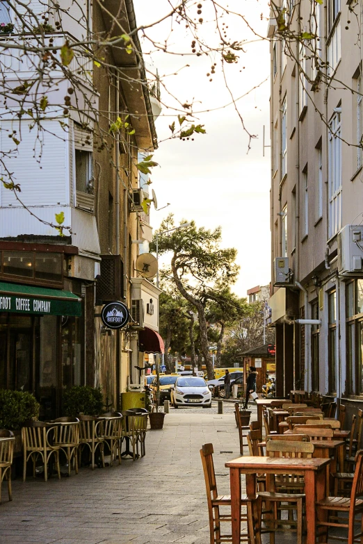 a street with several tables, chairs, and trees lining the side of it