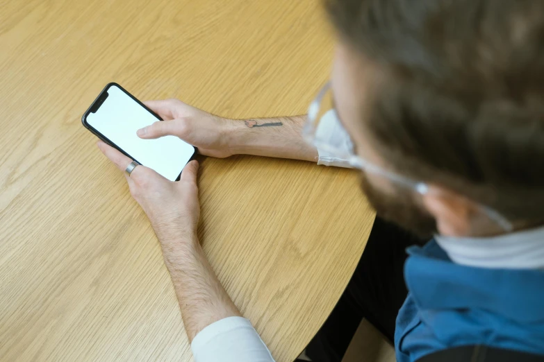 a man with a face mask sitting at a wooden table while looking at a cell phone