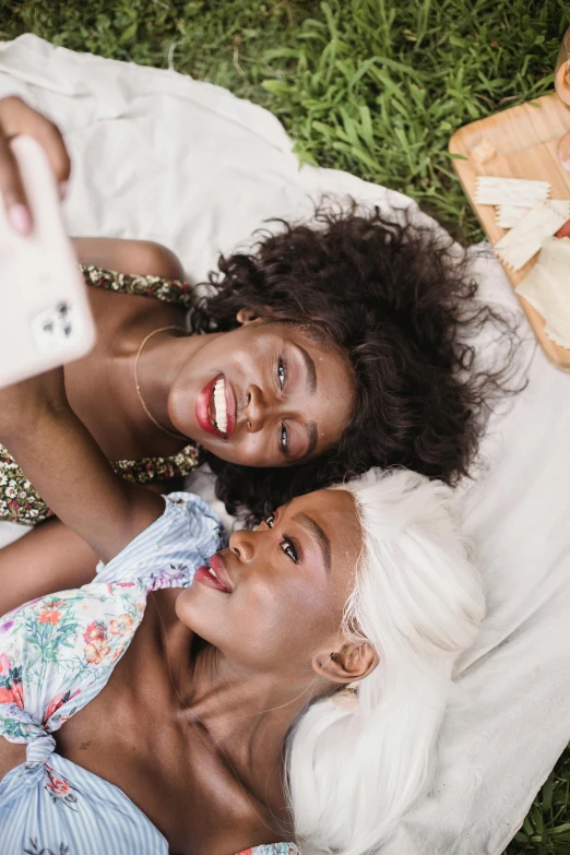 two women lying on a blanket with food in a wooden tray